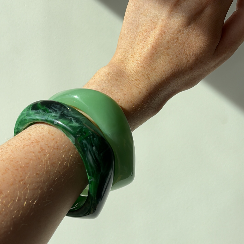 Hand wearing a green bracelet on a light background