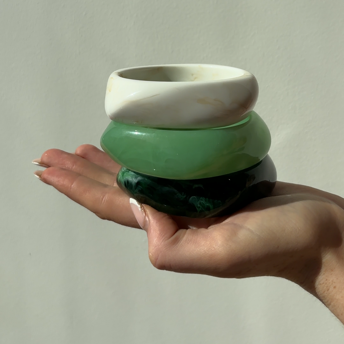 Hand holding a green and white bangles against a plain background